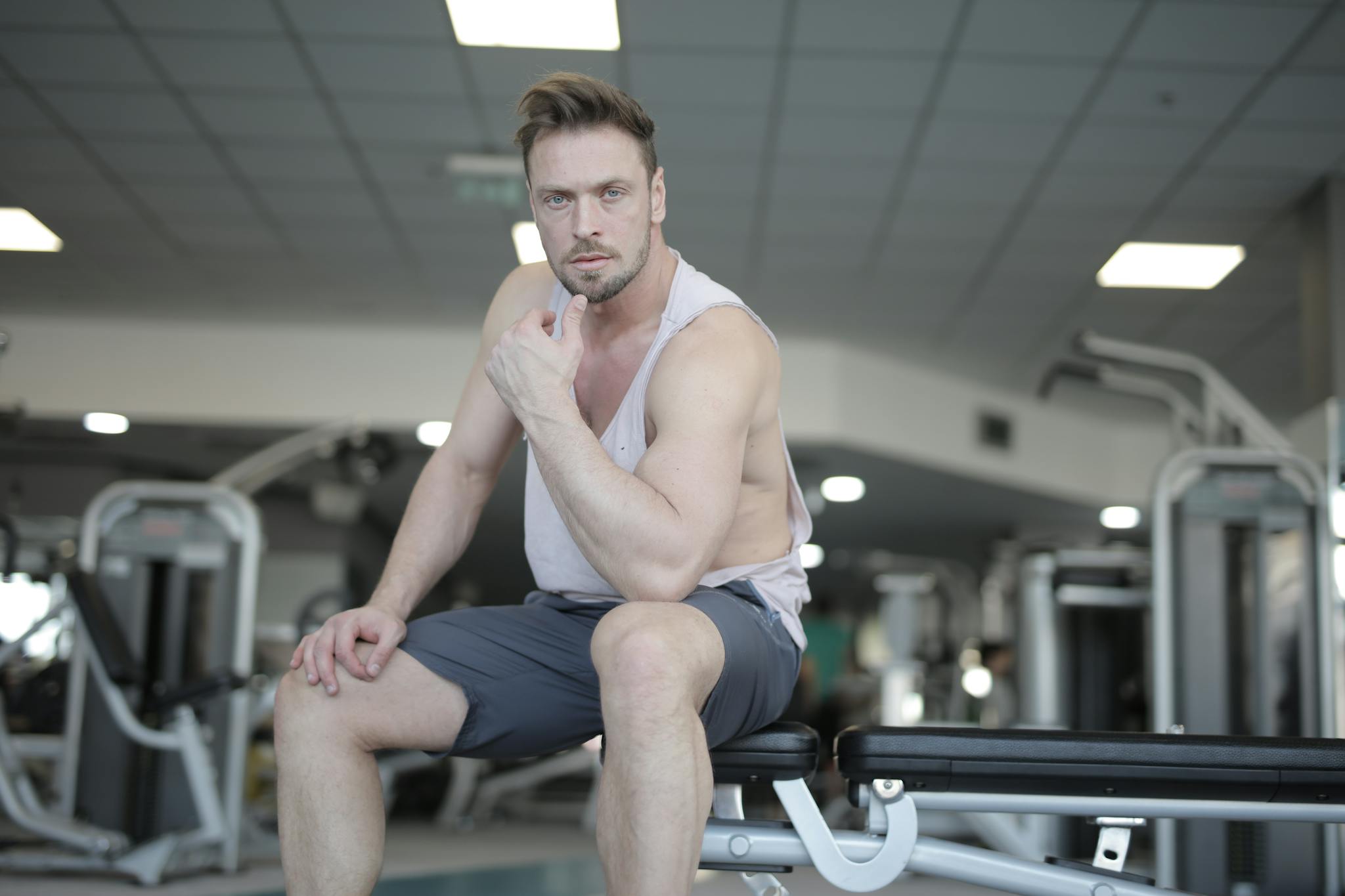 Focused young sportsman resting on bench after workout in fitness club